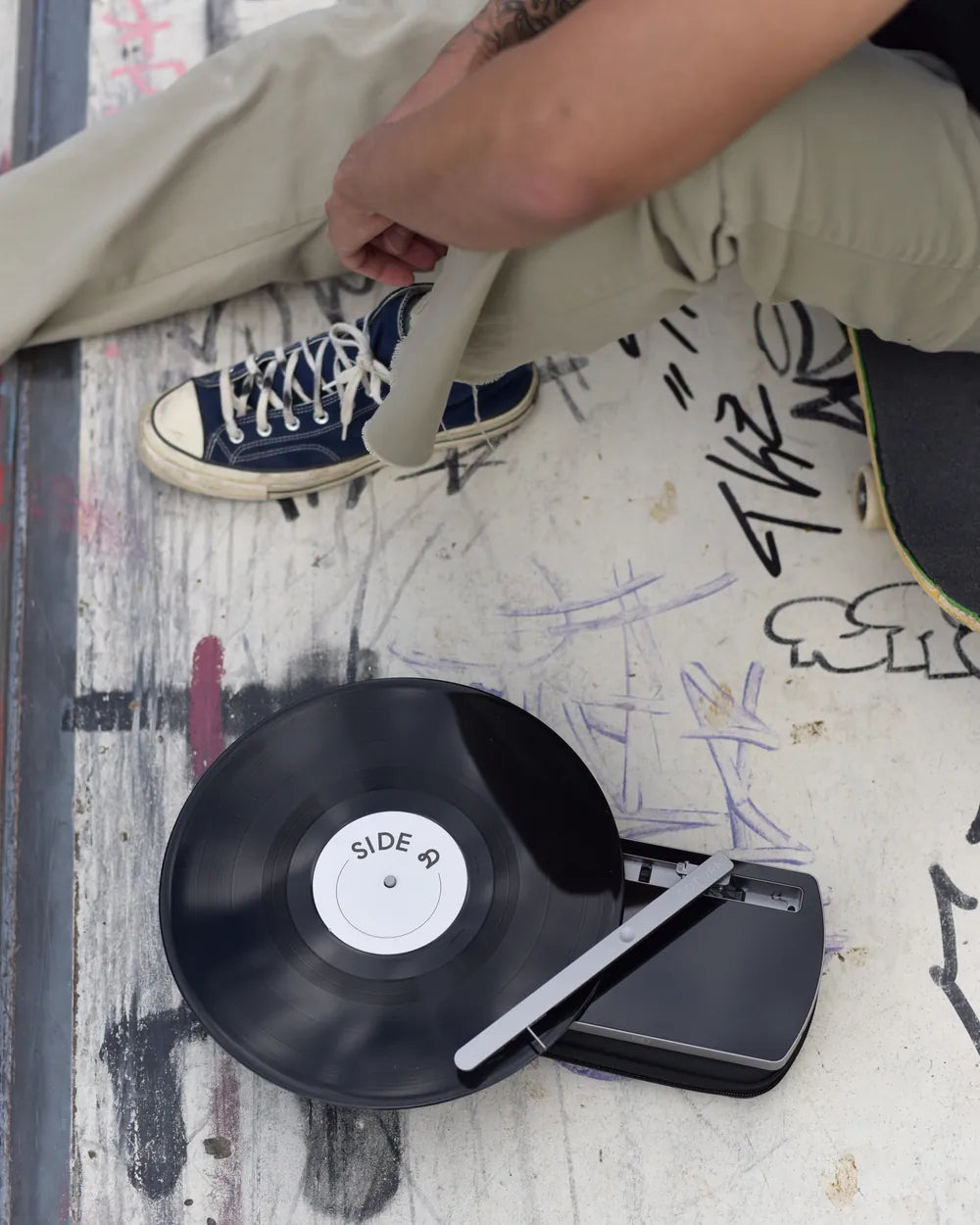 Der CT-TWO mit Platte auf einer bemalten Mauer, daneben Sneaker und ein Skateboard