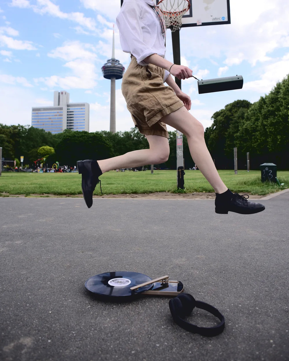 Eine Frau springt auf einem Basketballplatz über den CT-TWO, der mit Platte und Kopfhörern auf dem Asphalt liegt